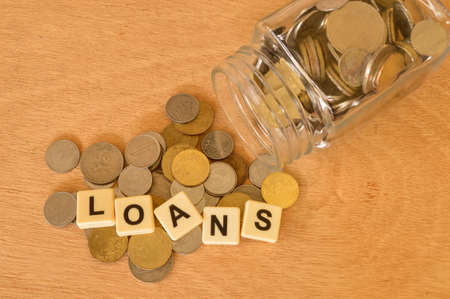 Stack of coins and square letters with text LOANS. Financial concept.