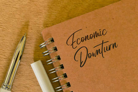 Phrase ECONOMIC DOWNTURN written on notebook with pen.の写真素材