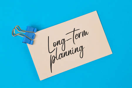 Phrase LONG - TERM PLANNING written on white paper over blue background.の写真素材