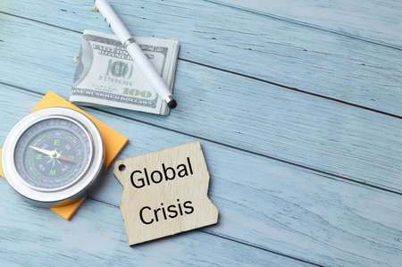Compass, pen, money banknotes and wooden board written with GLOBAL CRISIS.の写真素材