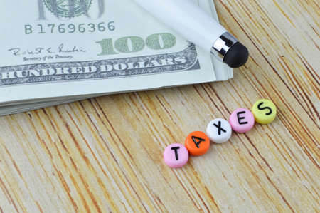 Pen, money banknotes and alphabet beads with word TAXES.の写真素材