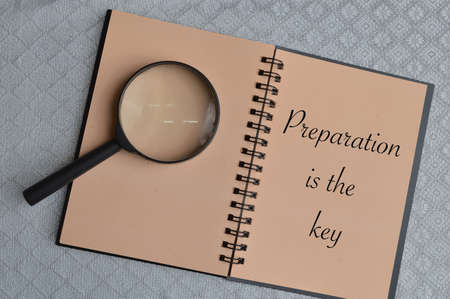Top view of magnifying glass and notebook written with text PREPARATION IS THE KEY.の写真素材