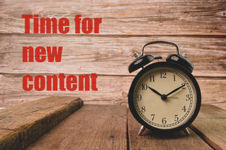 Alarm clock on wooden board with text TIME FOR NEW CONTENT.の写真素材
