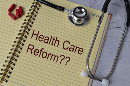 Top view of stethoscope, pill capsules and notebook written with text HEALTHCARE REFORM?の写真素材