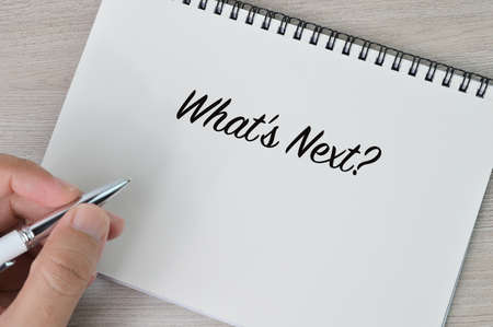 Hand holding pen and writing text WHAT'S NEXT?