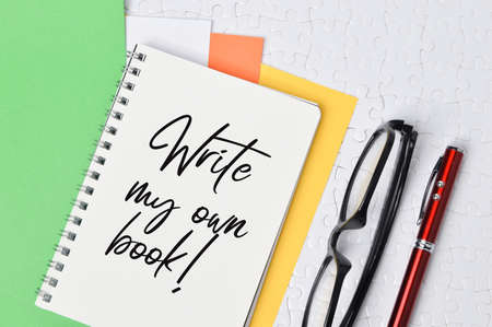 Top view of pen, eyeglasses and notebook written with WRITE MY OWN BOOK!
