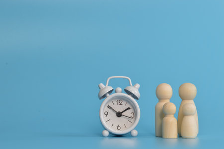 Family doll figures with clock on blue background. Family time concept.の写真素材