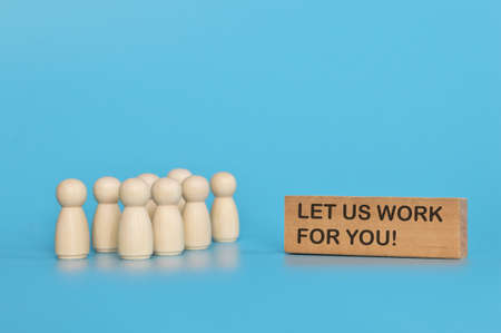 Wooden doll figures standing in front of the wooden block written with LET US WORK FOR YOU?の写真素材
