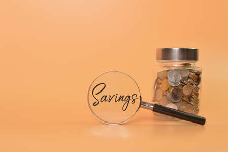 Bunch of coins in a glass jar and magnifying glass with text SAVINGS.の写真素材