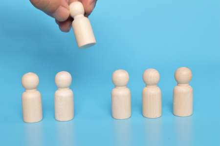 Hand grabs wooden doll figure from the group of workers. Firing someone concept