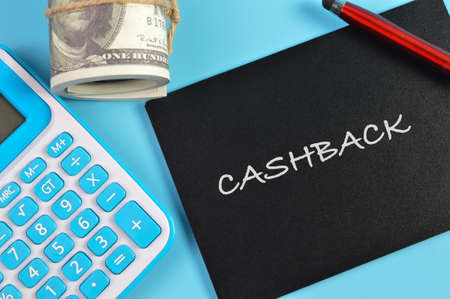Top view of pen, money banknotes, calculator and chalkboard written with CASHBACK.