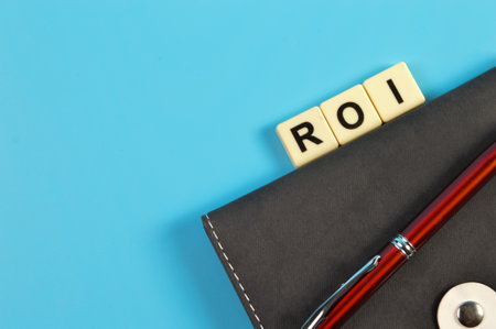 Top view of pen, notebook and square letters with text ROI stands for Return On Investmentの写真素材