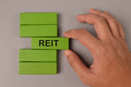 Hand picked wooden block written with REIT stands for Real Estate Investment Trust.の写真素材