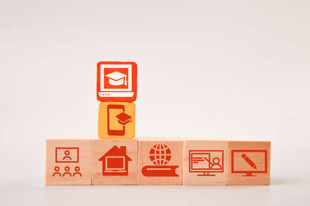 Graduation cap on red wooden block with students, classroom and computer symbolsの写真素材