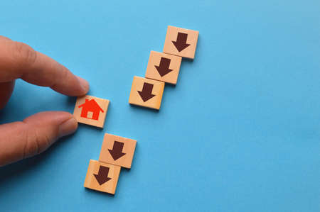 Hand picked home icon with an arrow down on wooden blocks. The fall and crisis of the real estate market.の写真素材