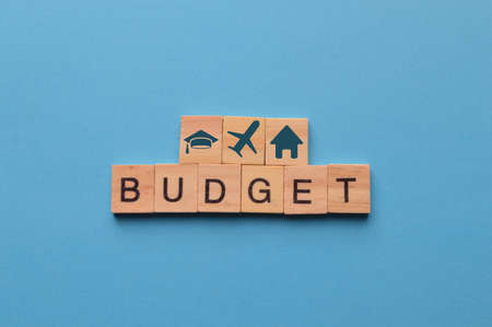Wooden blocks with graduation cap, plane, home icons and the word BUDGET. Monthly expenses concept.の写真素材