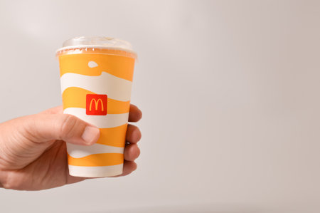 Klang, Malaysia: June 24, 2021- Hand holding McDonald's soft drink in paper cup isolated on grey...