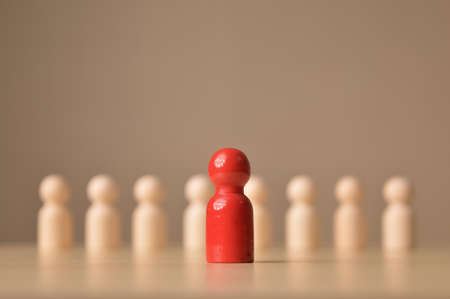 Red wooden doll figure standing out from the crowd. Blurred backgroundの写真素材