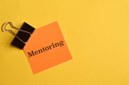 Orange paper written with text MENTORING isolated on yellow background