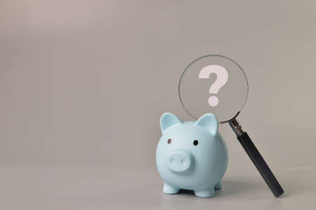 Piggy bank and magnifying glass with question mark symbol. Copy spaceの写真素材