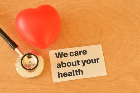 Red heart shape, stethoscope and white paper with phrase WE CARE ABOUT YOUR HEALTHの写真素材
