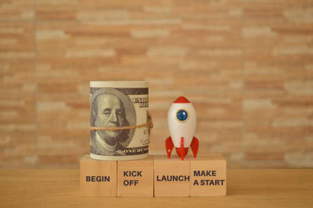 Toy rocket and money banknote with phrase BEGIN, KICK OFF, LAUNCH and MAKE A STARTの写真素材