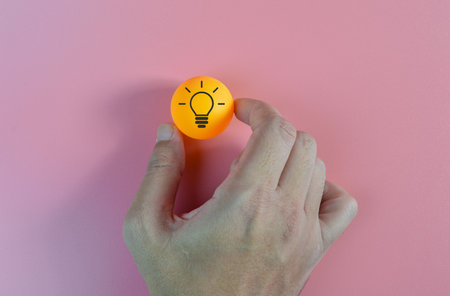 Hand holding an orange ball with light bulb symbols