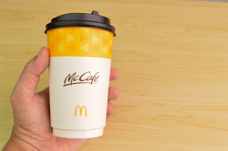 Klang,Malaysia: July 25, 2021- Hand holding McCafe coffee drink cup isolated on wooden backgroundのeditorial素材