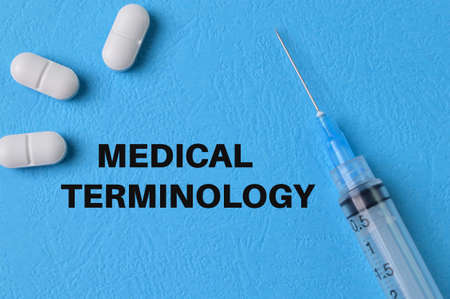 Syringe injection and pill capsules on blue background with text MEDICAL TERMINOLOGYの写真素材