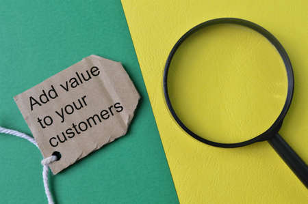 Magnifying glass and label tag written with ADD VALUE TO YOUR CUSTOMERSの写真素材