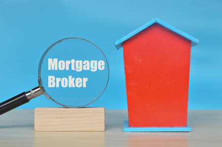 Toy house and magnifying glass with text MORTGAGE BROKER