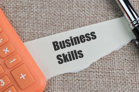 Pen, calculator and torn paper written with BUSINESS SKILLS