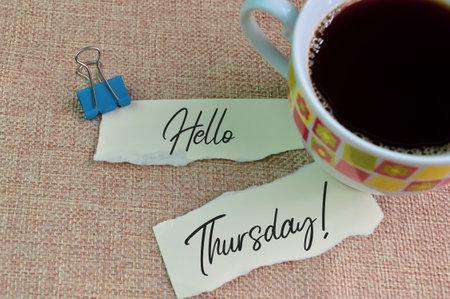 A cup of coffee and torn papers with text HELLO THURSDAYの写真素材