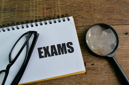 Eyeglasses, magnifying glass and notebook written with text EXAMS