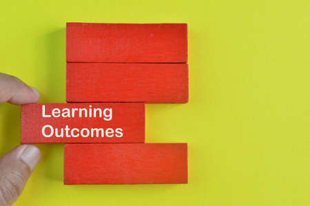 Hand picked wooden block written with text LEARNING OUTCOMES