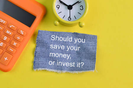 Clock, calculator and ripped pieces of jeans with question SHOULD YOU SAVE YOUR MONEY, OR INVEST IT?の写真素材
