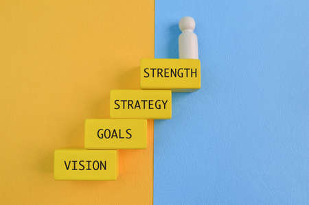 Wooden people figure standing on wooden blocks with text STRENGTH, STRATEGY, GOALS and VISIONの写真素材