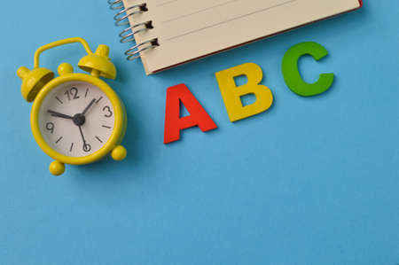 Clock, notebook and ABC letters isolated on a blue background with copy spaceの写真素材