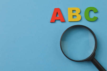 Magnifying glass and ABC letters isolated on a blue background with copy spaceの写真素材