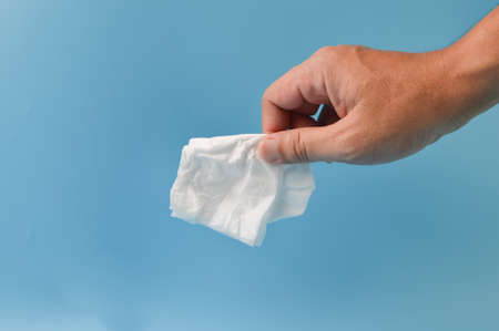 Hand holding crumpled tissue paper isolated on a blue backgroundの写真素材