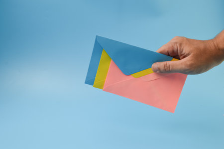 Hand holding colorful envelopes isolated on a blue backgroundの写真素材