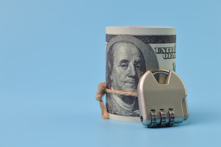 Money banknote and padlock isolated on a blue background. Concept security of money and compensation for losses in inflationの写真素材