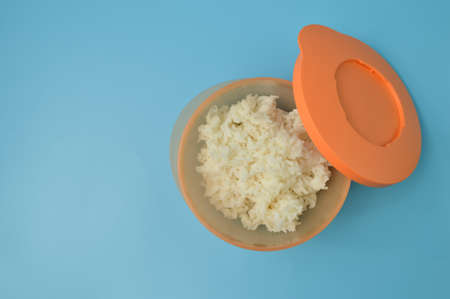 Cooked white rice in a plastic bowl isolated on a blue background
