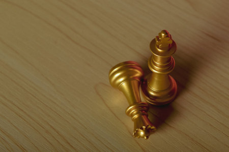 Gold king chess piece win over lying down yellow queen on wooden backgroundの写真素材