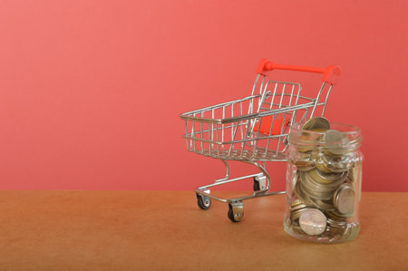 A shopping trolley and coins are a symbolic representation of spending money in shops or making advantageous purchases in shopping centers using currency.の写真素材