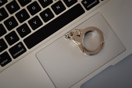 Top view of handcuffs and laptop. the image of handcuffs hanging above a notebook keyboard represents the business concept of punishment. Online piracy, fraud phishing, internet safety, web security, hackingの写真素材