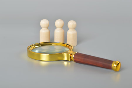 Magnifying glass and wooden figure.Embark on a talent-hunting adventure with the concept of recruitment, as symbolized by a magnifying glass. Dive into the pool of potential candidates, examining their skills and qualifications closely to discover the ideal match for your teamの写真素材