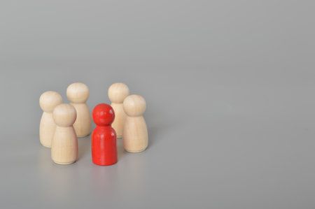 A circle of people surrounds a red person.This depiction represents the essence of business teamwork, showcasing the power of collaboration, team spirit, and collective effort. The wooden figures of people symbolize the strength and unity that arise through discussion, cooperation, and selective focus on shared goalsの写真素材