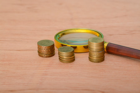 A magnifying glass placed upon a bed of coins, symbolizing financial development, banking accounts, statistical analysis, investment research, and stock exchange trading.の写真素材