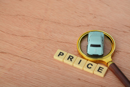 Magnifying glass and toy car with text PRICE. Delving into the concept of the expanding transport market and the resulting fluctuations in car prices.の写真素材